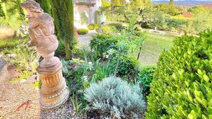 Ein Garten mit einer Statue, ein Gebäude mit einem Balkon und verschiedene Pflanzen.