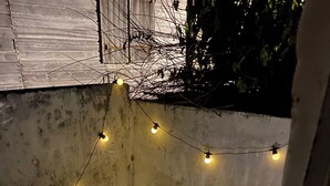 A small outdoor seating area with a chair and a table, string lights, and a potted plant.