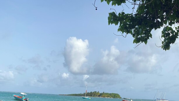 A beach with boats, a sandy shore, and a distant island.