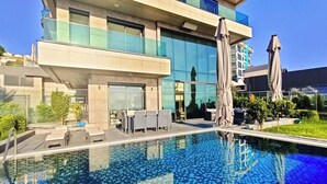 A modern hotel with a swimming pool, outdoor seating, and a large glass facade. - Luxury villa with sea view & 9,000 m² SPA access (Kargıcak)