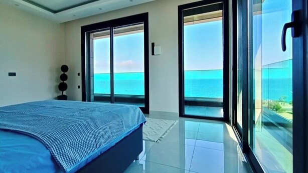 A bedroom with a large bed, a view of the sea through glass doors, and a modern design. - Luxury villa with sea view & 9,000 m² SPA access (Kargıcak)