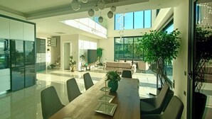 A modern dining area with a long wooden table, black chairs, and a large potted plant. - Luxury villa with sea view & 9,000 m² SPA access (Kargıcak)