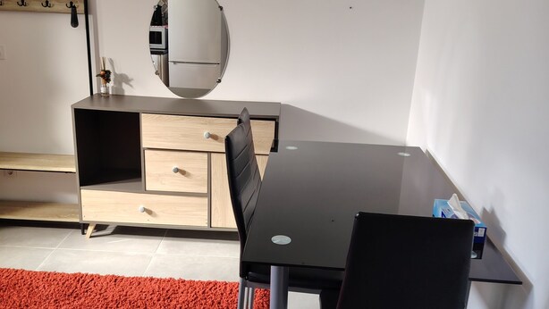 A modern room with a black dining table, two chairs, a red carpet, a wooden cabinet, and a mirror on the wall.