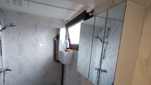 A bathroom with a marble wall, a sink with a mirror above it, and a window above the mirror.