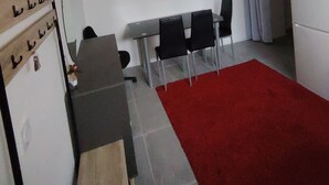 A compact kitchen with a dining area, a red carpet, and a wall-mounted shelf with hanging items.