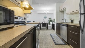 Une cuisine moderne équipée d’un four, d’un micro-ondes et d’un réfrigérateur encastrés. On y trouve un coin repas avec une table et des chaises, ainsi qu’un petit tapis sur le sol.