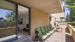 Un espace extérieur aménagé avec des chaises rembourrées de couleur verte et une table, une porte-fenêtre coulissante donnant sur un espace intérieur, et un mur en briques.
