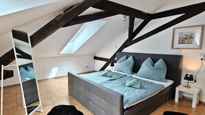 A bedroom with a sloped ceiling, a bed with blue bedding, a nightstand with a lamp, and a framed picture on the wall.