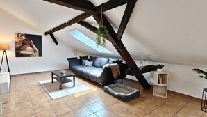 A modern loft apartment with exposed wooden beams, a grey sofa, a small coffee table, and a pet bed.
