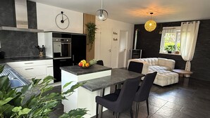 A modern kitchen with a central island, black chairs, and a dining table. There is a sofa and a small table in the living area. - At the Secret Garden (Rimsdorf)