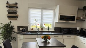 A modern kitchen with a central island, black chairs, a dining table, a microwave, and a sink. - At the Secret Garden (Rimsdorf)