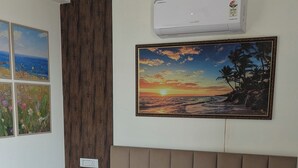 A bedroom with a bed, a nightstand, a wall-mounted air conditioner, and framed artwork.