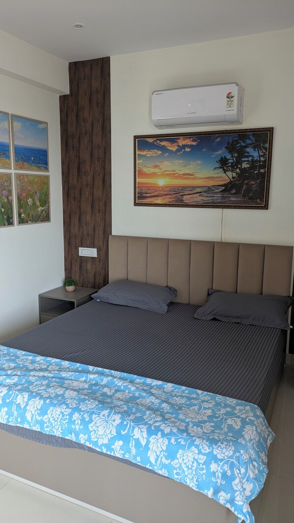 A bedroom with a bed, a nightstand, a wall-mounted air conditioner, and framed artwork.
