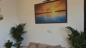 A living room with a beige sofa, a coffee table, a ceiling fan, and a painting of a sunset.