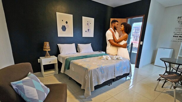A hotel room with a bed, a nightstand, a chair, and a small table. - 🏡 Roots Inn of Porto! Always ready to welcome you with affection💛📍 (Porto de Galinhas Ipojuca)