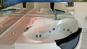 A spa area with a large bathtub, a mirror, and a mural of a waterfall. - Dream Inn (Inglewood)