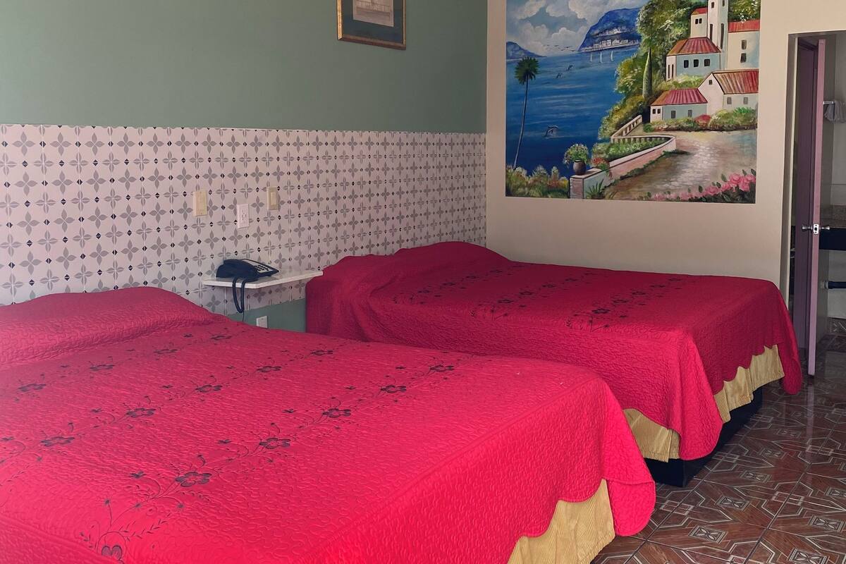 Hotellihuone, jossa on kaksi sänkyä, merimaiseman kuvaava taulu ja kuviollinen tapetti.