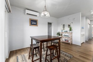 Ein Essbereich mit einem Holztisch, Barhocker, einer hängenden Pendelleuchte und einem gemusterten Teppich.