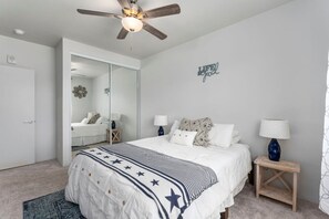 Ein Schlafzimmer mit Bett, Nachttischen, Deckenventilator, Kleiderschrank und Spiegel.