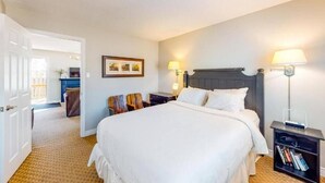 A hotel room with a large bed, a bedside table with a lamp, a small desk with a chair, and a bookshelf. - Steps to the Hill 1 Bedroom Wifi Crave TV (Blue Mountain)
