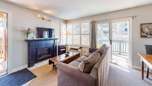 A living room with a fireplace, a sofa, a television, and a large window. - Steps to the Hill 1 Bedroom Wifi Crave TV (Blue Mountain)