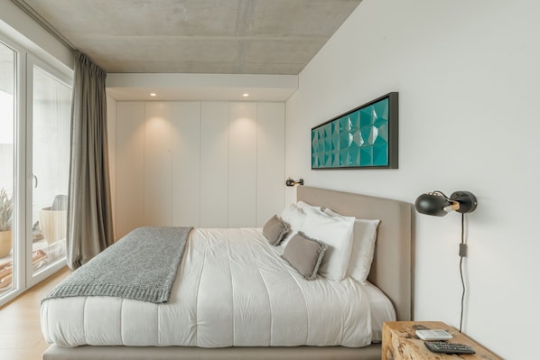 A modern bedroom with a large bed, a bedside table with a lamp, and a view through a sliding door to a balcony. - Beach SUN Apartment by Vacationy (Vila Nova de Gaia)