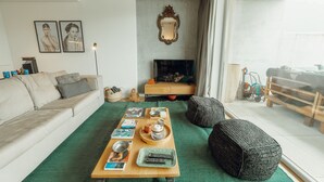 A living room with a green carpet, a wooden coffee table, a sofa, a TV, and a large mirror on the wall.