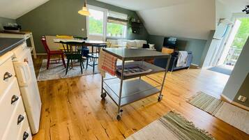 A compact kitchen with a dining area, a TV, and a window with a view of greenery.