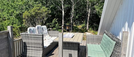 A wooden deck with wicker furniture, including a sofa and chairs, and a table with cups and a tray.