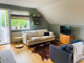 A living room with a white sofa, a grey sofa, a television, a wooden cabinet, a brown furry rug, and a window with blinds. - 4 Person Holiday Home in Nosund (Nosund)