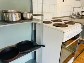 Una cocina con estufa blanca, dos ollas sobre la encimera y una sartén en el estante del horno.