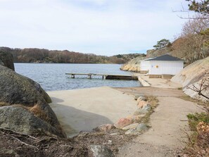 Een betonnen steiger die in een meer uitstelt, omringd door rotsen en een klein wit gebouw met een dak.
