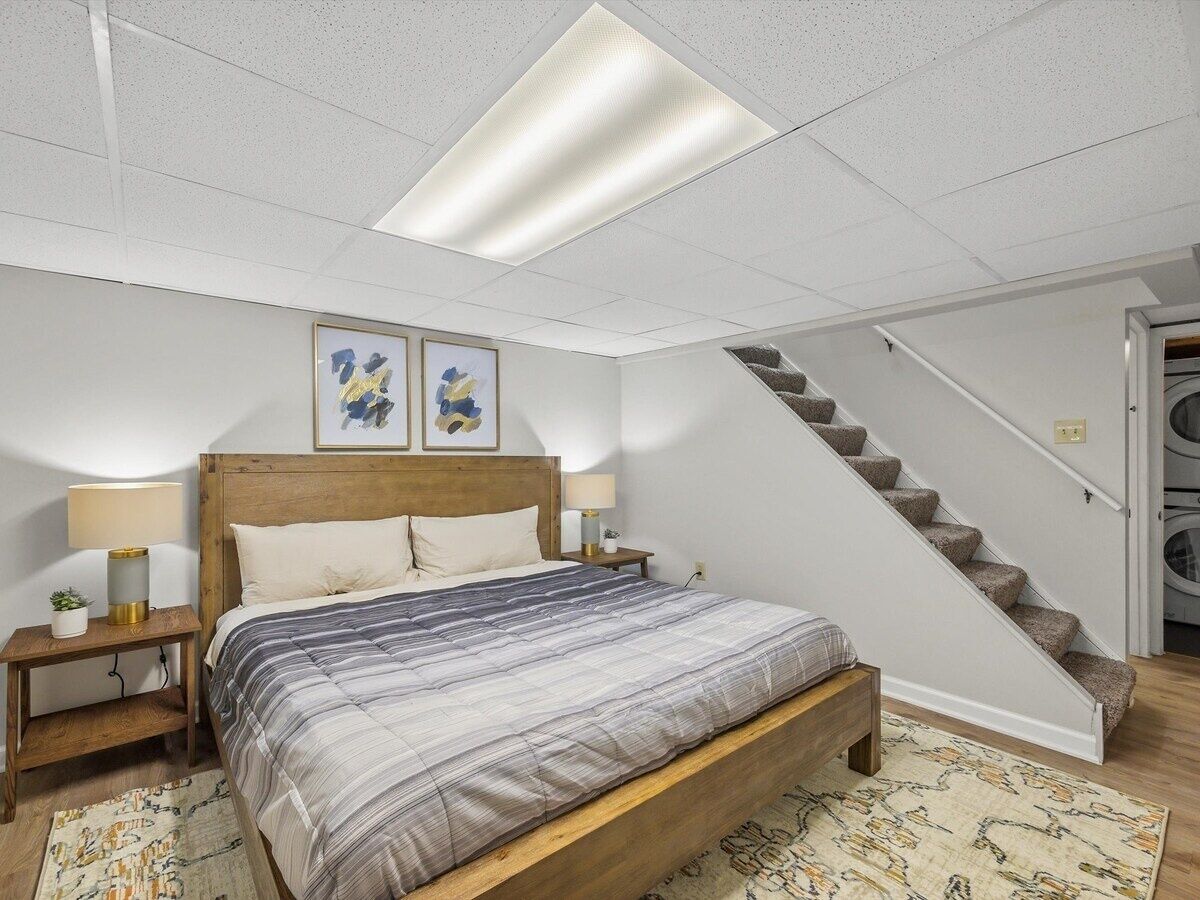 A bedroom with a bed, nightstands, a headboard, a staircase, and a ceiling light.