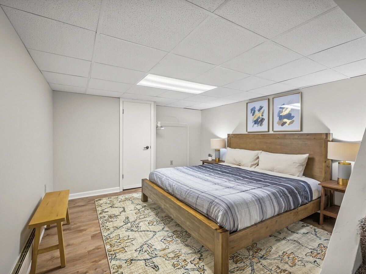 Een slaapkamer met een houten bed, nachtkastje, bankje en een deur.