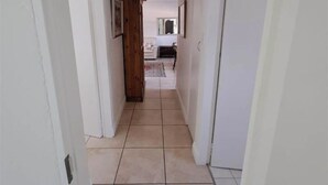 Un estrecho pasillo con paredes blancas y suelo de baldosas que lleva a una habitación con cama y ventana.