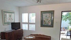 Una sala de estar con televisor, un mueble de madera, una mesa redonda de centro, una alfombra estampada, un sofá y un cuadro en la pared.
