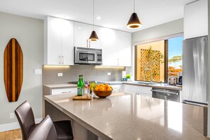 A modern kitchen with white cabinets, a large island, a microwave, and a refrigerator.