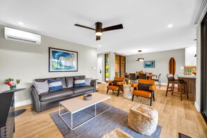 Ein modernes Wohnzimmer mit einem grauen Sofa, orangefarbenen Sesseln, einem Couchtisch und einem Deckenventilator.