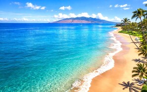 Une plage à l’eau turquoise et limpide, un rivage sablonneux et une montagne en arrière-plan.