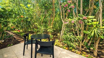 An outdoor seating area with a table and chairs, surrounded by dense tropical foliage and plants.