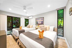 Quarto de hotel com duas camas, um ventilador de teto, uma janela grande com vista para o verde e um ar condicionado.