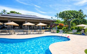 A swimming pool with lounge chairs and umbrellas, a covered seating area, and lush greenery.
