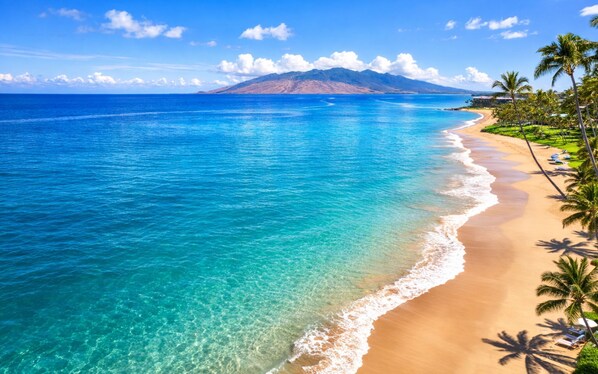 A beach with clear turquoise water, a sandy shore, and a mountain in the background.
