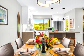 Una cocina moderna con vistas a un paisaje verde, un comedor con mesa dispuesta para seis personas y un amplio ventanal.
