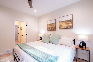 Un dormitorio con una cama grande, dos mesitas de noche con lámparas y dos cuadros enmarcados en la pared.