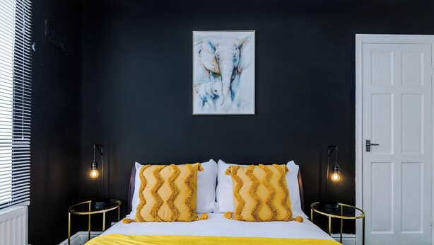 Un dormitorio con una cama, dos mesitas de noche, una puerta blanca y un cuadro en la pared.