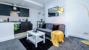 Un espacio moderno para vivir con cocina, un sofá gris, una mesa de centro blanca y una manta amarilla.
