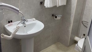 Une salle de bain équipée d’un lavabo sur colonne, d’une douchette à main, de toilettes et d’un porte-serviettes.