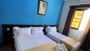 Une chambre d’hôtel avec deux lits, un mur bleu, un tableau et une fenêtre avec des rideaux.