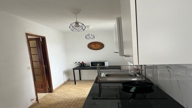 Une cuisine compacte avec un plan de travail noir, un évier et un four à micro-ondes. On y trouve une porte ornée d’un panneau décoratif et un luminaire au plafond.
